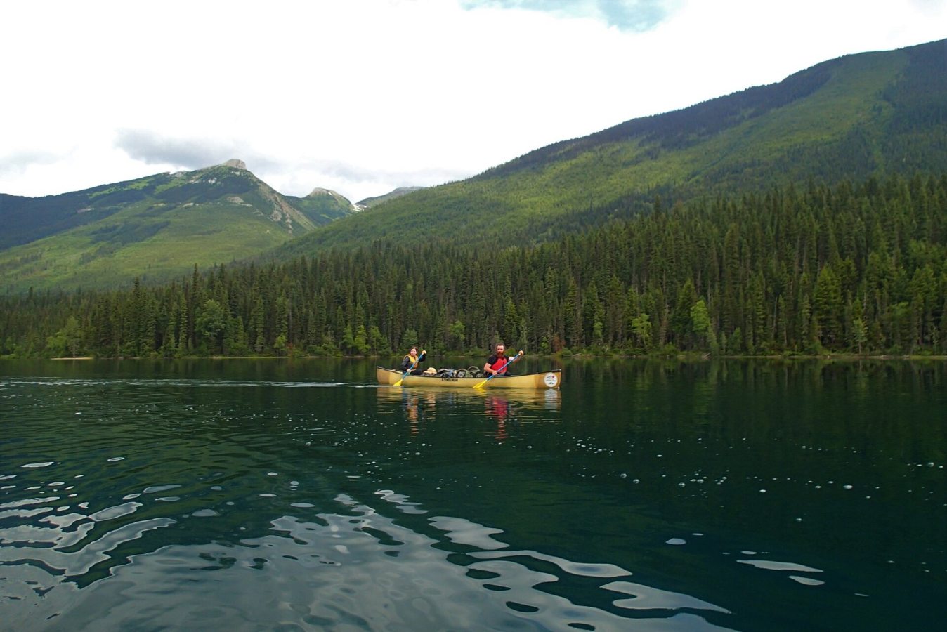 Two paddlers in a canoe in Bowron Lake Provincial Park, Cariboo mountains in background